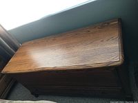 Blanket chest closed, showing medium brown wood grain surface and turned bun feet