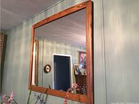 Wall-mounted rectangular mirror with wooden frame reflecting room interior