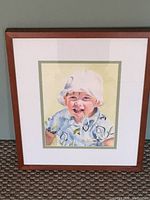 Photo of framed watercolour painting showing a young boy with white hat and blue patterned shirt.
