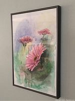 Frontal view of the framed watercolor painting showing three pink daisies against a soft blue-green background