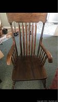 Front view of solid dark wood rocking chair showing vertical slat backrest, armrests, and seat.