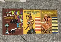 Photo showing three vintage craft books side by side on carpeted floor with covers visible.