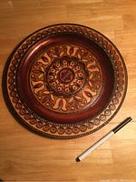 Top view of vintage hand made wooden decorative plate showing detailed hand painted patterns and rich color.