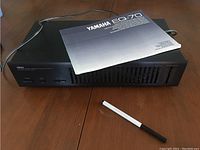 Yamaha EQ-70 graphic equaliser unit with manual placed on top and a pen for scale on wooden surface.