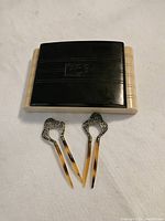 Closed view of the Bakelite playing card holder and two decorative Art Deco hair pins with tortoiseshell-patterned prongs.