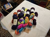 Overview of 12 skeins of assorted fingering weight wool yarn in varied vibrant and muted colors including multi-colors and solid shades displayed on white linen.