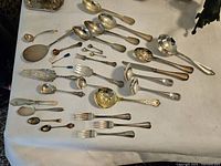 Overview of all flatware and serving utensils laid out on white cloth