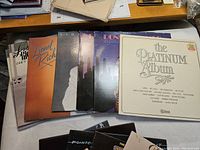 Top view of multiple vinyl record albums including Lionel Richie, Dionne Warwick, The Platinum Album, and others stacked on table.