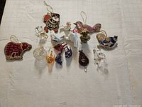Full view of 16 Christmas tree ornaments including glass and fabric styles with hanging strings on a white background