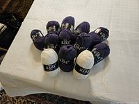 12 skeins of Drops Alaska wool yarn in purple and white colors arranged on a white cloth surface.