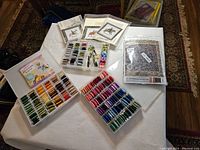 Wide top-down view of multiple trays filled with organized embroidery floss skeins alongside stacked packaged embroidery patterns and books on a table.