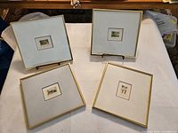 Four framed prints by Gingras-Hogue on white table. Each print is matted with wide white matte and narrow gold frames.