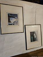 Two framed art prints lying on a white textured surface, showing one with a mountain and lake scene and the other with an abstract mountain scene.