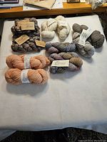 15 skeins of yarn arranged on white surface showing variety in color and brand.