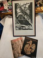 Framed black and white print and two books on Indigenous culture placed on a white surface