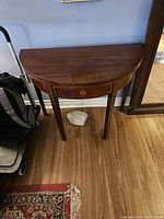 Closed semi-circular drop leaf table with dark wood finish and four legs.
