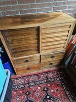 Front view of the wooden two-sided chest showing slatted doors and four drawers with metal handles.