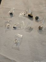 9 assorted jewelry pieces individually bagged laid out on fabric, including rings, pendants, and brooches in various designs and materials.