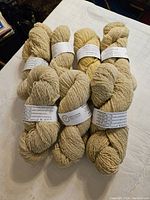 Eight skeins of cream colored 100% pure wool yarn laid out on a white surface, showing texture and size of yarn.