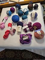 21 skeins and balls of various yarns in multiple colors laid out on table.