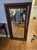 Full view of the mirror leaning against a wall showing the dark mahogany frame and reflective glass surface.