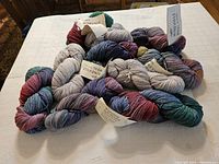 Group of ten skeins of multicolored 4 ply worsted wool yarn from Mineville Wool Boutique on white surface.