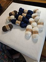 Overview of all wool skeins and balls in brown, indigo blue, and white colors arranged on white surface.