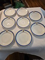Eight white luncheon plates with thick cobalt blue borders and gold accents displayed on white cloth.