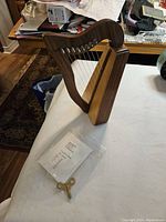 Mini harp standing on white surface, clear view of strings, wood frame, and tuning key on table nearby