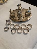 Full set arranged on a white cloth showing the metal tray with animal condiment holders and the napkin rings in front.
