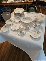 Full view of all 28 assorted porcelain Limoges dinnerware pieces set on a white cloth, showing plates, bowls, cups, and saucers with purple violets floral pattern and gold trim.