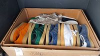 Wide view of cardboard box containing multiple pairs of adidas sneakers in various colors and materials