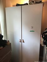 Front view of closed white IKEA wardrobe cabinet with two doors and leather handles.