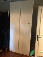 Closed white IKEA wardrobe cabinet standing upright, showing full height and double doors.