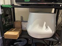 White Lomi composter on black metal shelf with cardboard Lomi box and white accelerator bag