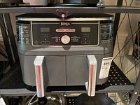 Front view of the Ninja air fryer showing the two cooking baskets with chrome handles, and the digital control panel with buttons and a central knob.