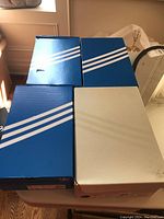 Four Adidas shoeboxes (three blue, one beige) on table