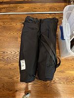 Two black rolled carrying bags lying side by side on wood floor