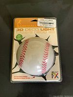 Photo of the baseball-shaped 3D deco light in its packaging showing brand, model, and baseball design.