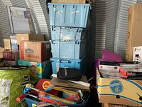 Overall lot showing stacked storage totes filled with miscellaneous items mixed with boxed items and some visible small items including backpacks and other gear.