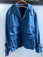 Front view of blue men's jacket showing collar, multiple button flap pockets, button cuffs, and shoulder button tabs.