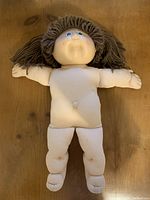 Full body front view of Cabbage Patch doll on wooden surface showing its body condition and hair.