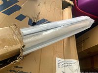 Partially opened box containing the roller shade wrapped in plastic, showing white components.