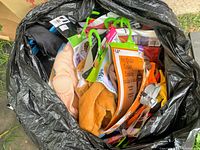 Garbage bag filled with multiple new costumes of various colors, styles and packaging. Visible are fabric pieces, costume masks, hangers, and character tags.