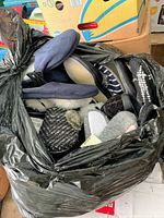 Black garbage bag filled with various new men's and women's slippers in assorted sizes and styles.