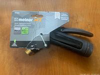 Photo of the Melnor XT200 rear trigger hose nozzle in its original packaging showing the black plastic handle and brass connector.