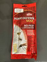 Photo showing the sealed red and white packaging of Ortho Home Defense Max No-Pest insecticide strip against a dark background.