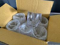 Box containing six large clear ribbed tumbler glasses, each wrapped in bubble wrap for protection.