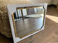 Mirror displayed on floor, showing dark faux marble frame with gold accents and corner protectors.
