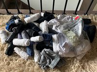 Photo showing a large assortment of rolled and loose men's and women's underwear on a carpeted floor. Includes various colors and brands visible in packaging and labels.